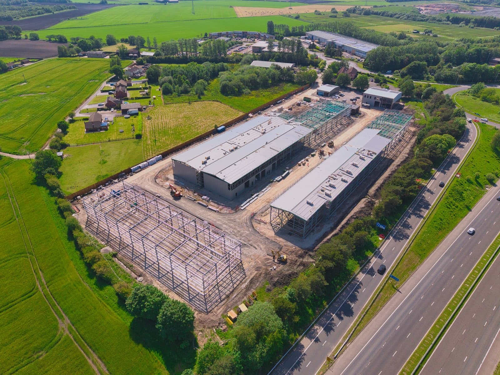 Drone aerial site survey of the Caddick Construction Tawd Valley Junction 4 scheme, Skelmersdale — showing portal-frame industrial units with steel erection complete and cladding works underway